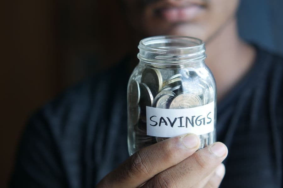 Savings Jar for Emergency Fund — 50/30/20 Budget Rule Person holding a glass jar labeled 'Savings' filled with coins — representing the 20% savings bucket in the 50/30/20 budget rule including the emergency fund
